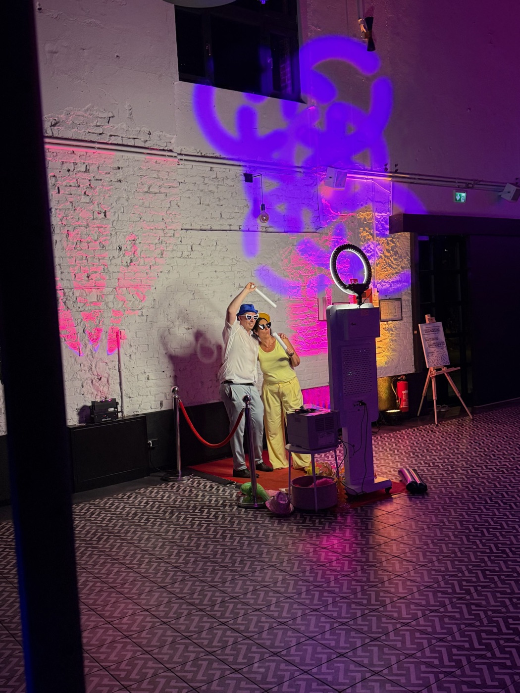 Zwei Gäste haben Spaß und feiern vor der Fotobox unter lila Licht